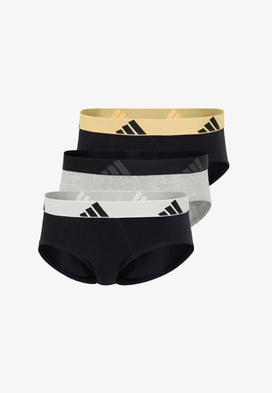 Athletischer schwarzer Mann steht barfuß, trägt schwarze Unterhosen mit einem gelben Bund und einem schwarzen Adidas-Logo.