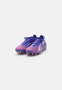 Scarpette da calcio viola e rosa con parte superiore testurizzata, chiusura con lacci e suola con tacchetti stampati. Presentano un accento bianco sul lato.