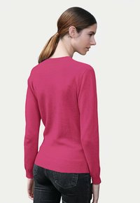 Pull rose cintré à manches longues et col rond. Texture douce et poignets côtelés. Porté avec un jean foncé, vu de dos.