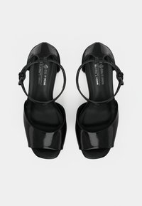 Μαύρα vegan σανδάλια με γυαλιστερό φινίρισμα, σχέδιο ανοιχτού δαχτύλου και λεπτό λουράκι στον αστράγαλο. Διαθέτουν καμπυλωτή μπροστινή λωρίδα και λεία σόλα.