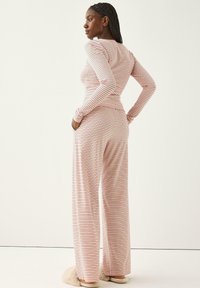 Stribet loungewear sæt i blødt pink og hvidt stof. Langærmet top med tætsiddende design, vide bukser med elastisk talje.