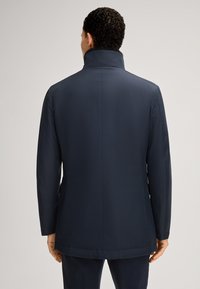 Marineblauwe jas met een hoge kraag, met een gladde textuur en een getailleerde pasvorm. Eenvoudig ontwerp met een rechte rug en zonder zichtbare sluiting.