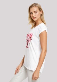 White cotton t-shirt featuring a red and pink tree design with heart-shaped leaves, short rolled sleeves, and a relaxed fit.