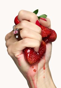 Hand houdt drie rode aardbeien vast en knijpt erin zodat het sap vrijkomt, met een glanzende textuur; vergezeld door zilveren en roze ringen. Witte achtergrond.