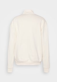 Sudadera color crema con un cuello alto, hombros caídos y puños ajustados. Textura suave sin patrones visibles ni herrajes.