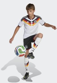 White soccer jersey with red, yellow, and black chevron pattern, black shorts, striped socks, and black cleats, with a colorful soccer ball.