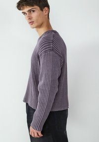 Lila gerippter Pullover mit langen Ärmeln, runder Ausschnitt und kontrastierenden Texturen an den Schultern. Der Saum ist leicht verkürzt.