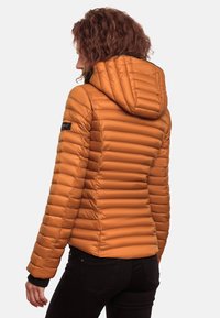 Oranž puffer jakk, horisontaalne tikand, vormitud kapuuts ja mustad varrukad. Eristav element on bränditud patch vasakul käel.