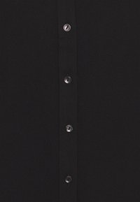 Tissu noir avec une rangée verticale de cinq petits boutons ronds brillants cousus au centre.