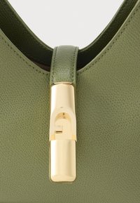 Πράσινη δερμάτινη τσάντα με λεία υφή, που διαθέτει κούμπωμα από μεταλλικό εξάρτημα σε χρυσό χρώμα και μοναδικό γεωμετρικό διακοσμητικό στοιχείο.