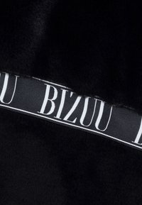 Czarna tkanina z sztucznego futra o gładkiej teksturze i błyszczącym wykończeniu, z czarną wstążką z białym napisem "BIZOU" jako akcentem.