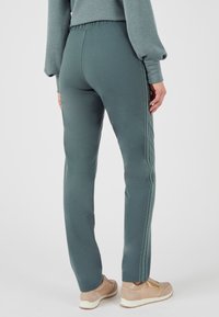Salie groene sweatpants met een getailleerd ontwerp, elastische tailleband, zijnaaddetail en een zachte textuur, gecombineerd met lichtbruine sneakers.