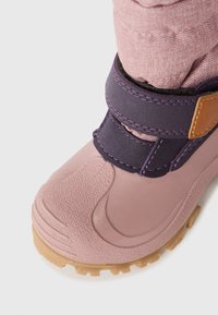 Rozā gumijas zābaks ar teksturētu apdari, purpura auduma apkakle, Velcro josta un bēša gumijas zole ar trieciena rakstu.