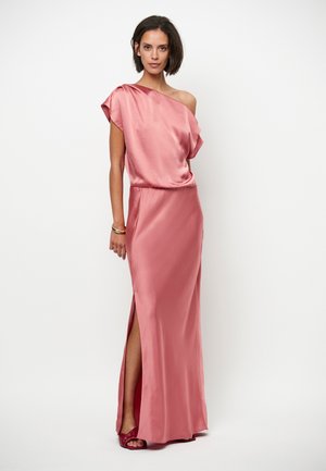 Robe en satin rose avec une épaule dénudée, une fente latérale et une taille froncée. Le tissu, lisse et brillant, tombe jusqu'au sol.