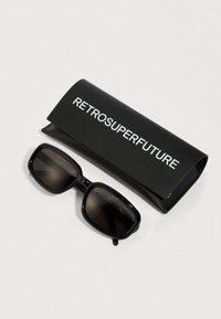 Sorte rektangulære solbriller med gradientlinser ved siden af et sortetui med teksten "RETROSUPERFUTURE" i hvid. Glat, blank overflade.