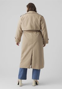 Beige trenčkot s Crop designem, s rozparkem na zádech, páskem v pase a knoflíkovými manžetami, doplněný širokými džíny a botami na podpatku.
