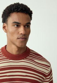 Rot-weiß gestreifter Strickpullover mit einem gerippten Rundhalsausschnitt. Nahaufnahme eines männlichen Models, das die Textur und Design-Details des Kleidungsstücks zeigt.