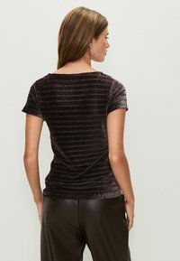 Sötétbarna, rövid ujjú felső textúrázott, bordázott mintával. Puha anyaga simán hullik, kerek nyakkivágással és enyhén testhezálló formával.