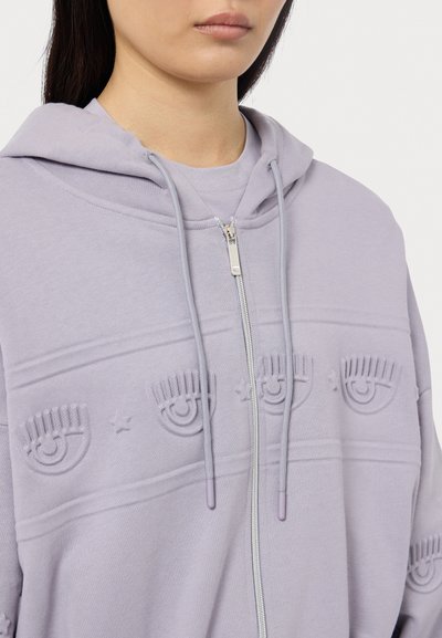 Felpa com fecho éclair em lavanda clara, feita de algodão macio. Apresenta designs de olhos em relevo e estrelas no peito. Capuz com cordão e fecho éclair prateado.