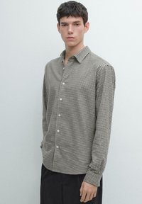 Camicia da uomo a maniche lunghe con motivo a quadri verde scuro e bianco, caratterizzata da collo alla coreana e chiusura frontale con bottoni. Tessuto dalla trama liscia.