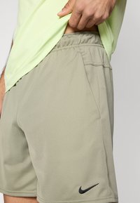 Hellgraue Sportshorts mit elastischem Bund und einem kleinen schwarzen Nike-Logo an der unteren linken Seite. Glatte Textur.