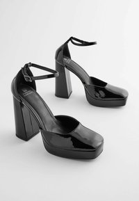 Talons plateforme en cuir verni noir avec un bout carré, une bride de cheville et un large talon bloc. Finition brillante avec semelle intérieure rembourrée.