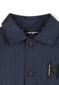 Chemise en denim pour enfants de couleur bleu foncé, arborant un col classique, des boutons noirs et un logo brodé. Texture lisse avec un motif de tissage subtil.