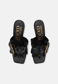 Chinelos pretos com uma alça suave e ondulada e detalhe de fivela em tom de ouro. Apresenta uma ponta quadrada e palmilha almofadada.