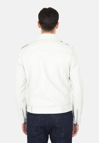 Giacca di pelle bianca con colletto a punta, tasche laterali con zip e polsini con zip, caratterizzata da una texture liscia e un design aderente.