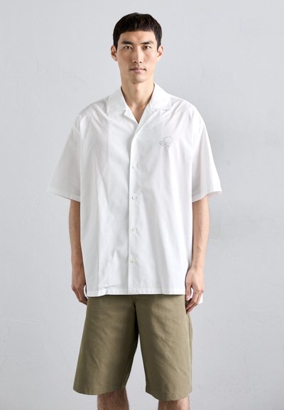Chemise blanche à manches courtes avec une coupe décontractée, fabriquée en coton. Présente un petit détail brodé sur la poitrine. Associée à un short en khaki.