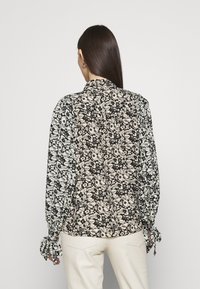 Chemise à manches longues avec un imprimé floral noir et blanc. Tissu doux, coupe ample, avec des poignets noués et un col classique.