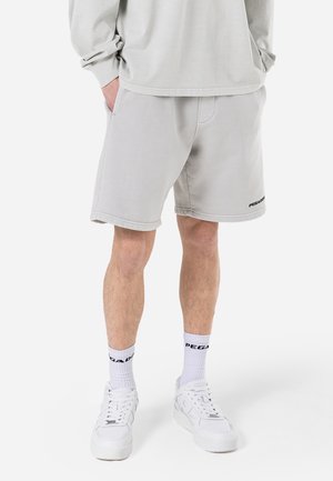 Graue Shorts aus einem Baumwollmischgewebe mit elastischem Bund und Seitentaschen. Ergänzt durch weiße Sportschuhe und Socken mit Logodruck.