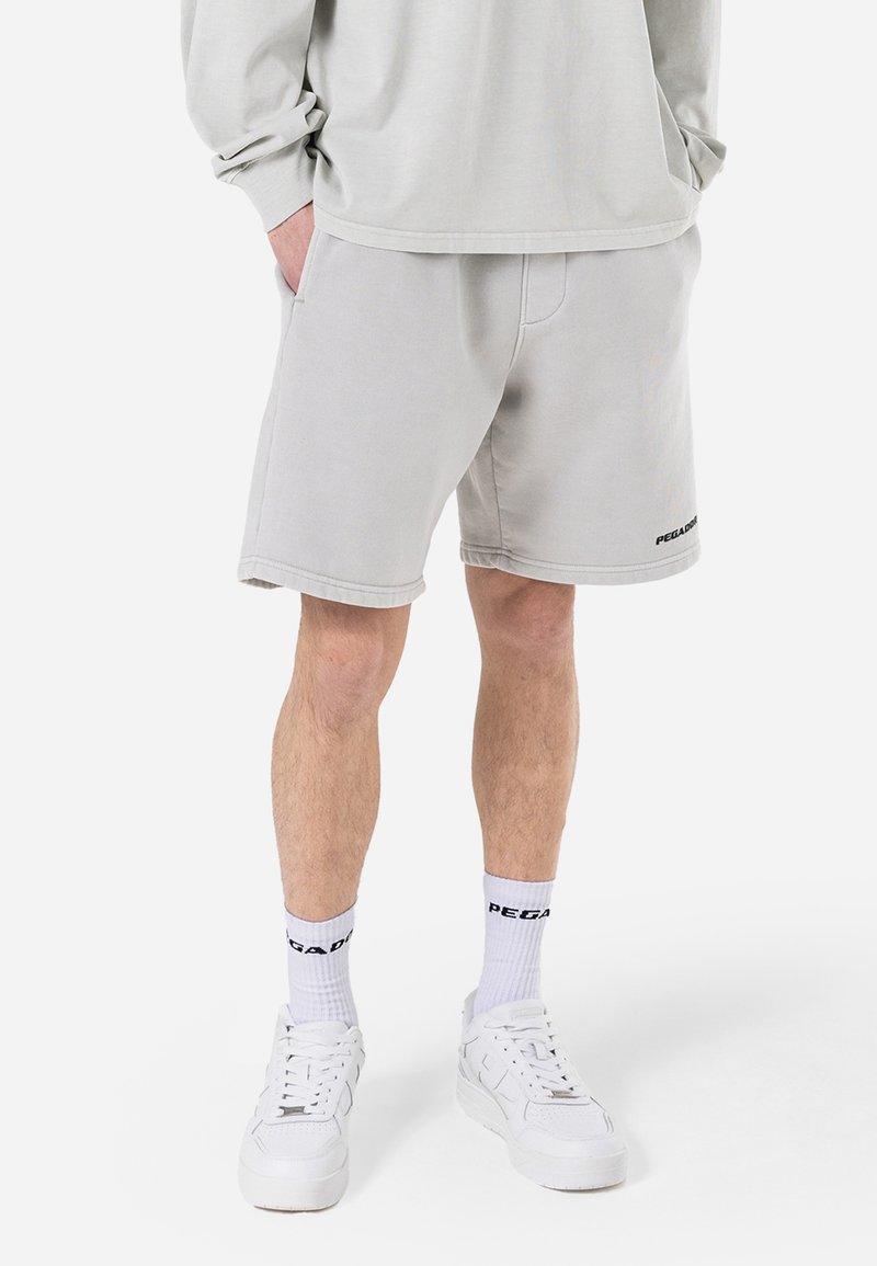 Shorts gris en mélange de coton avec une ceinture élastique et des poches latérales. Complétés par des chaussures de sport blanches et des chaussettes à logo imprimé.