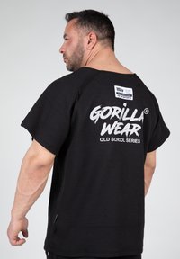Zwarte korte mouwen shirt met een gestructureerde stof. Kenmerkt zich door een groot wit "GORILLA WEAR OLD SCHOOL SERIES" logo op de achterkant en een label op de nek.