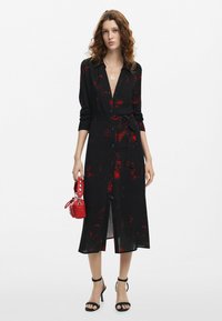 Mustmustaline must kleid punaste lillemotiividega, nupud ees ja seotud vöö. Koos mustade kontsade ja väikese punase käekotiga.