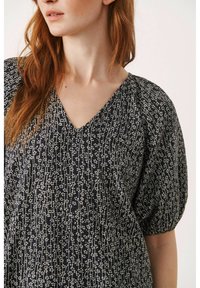 Blusa de estampado en blanco y negro con escote en V, mangas cortas abullonadas y tejido suave. Presenta un diseño texturizado de líneas verticales y puntos.