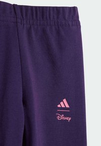 Pantaloni sportivi viola con una consistenza morbida. Presentano un logo Adidas rosa e il testo "Disney", con una vita elastica per il massimo comfort.
