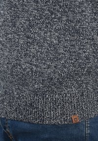Pull en tricot bleu marine et blanc avec un design texturé et un ourlet côtelé. Comprend une petite étiquette de marque en cuir marron en bas.