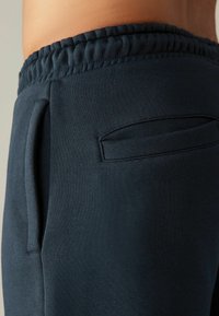 Pantalones deportivos de color azul oscuro con una cintura elástica, bolsillos laterales y una tela suave y texturizada. El diseño enfatiza la comodidad y la utilidad.