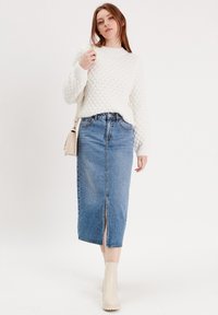 Pull en tricot blanc avec un motif texturé, associé à une jupe midi en denim bleu avec une fente à l'avant. Des bottines beige à la cheville complètent le look.