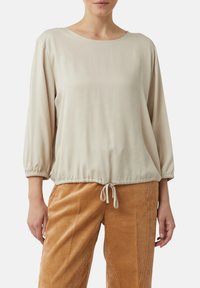 Beige Langarmshirt mit Rundhalsausschnitt und gerafften Bündchen, ausgestattet mit einem Kordelzugsaum und glattem Stoff. Kombiniert mit Cordhosen.