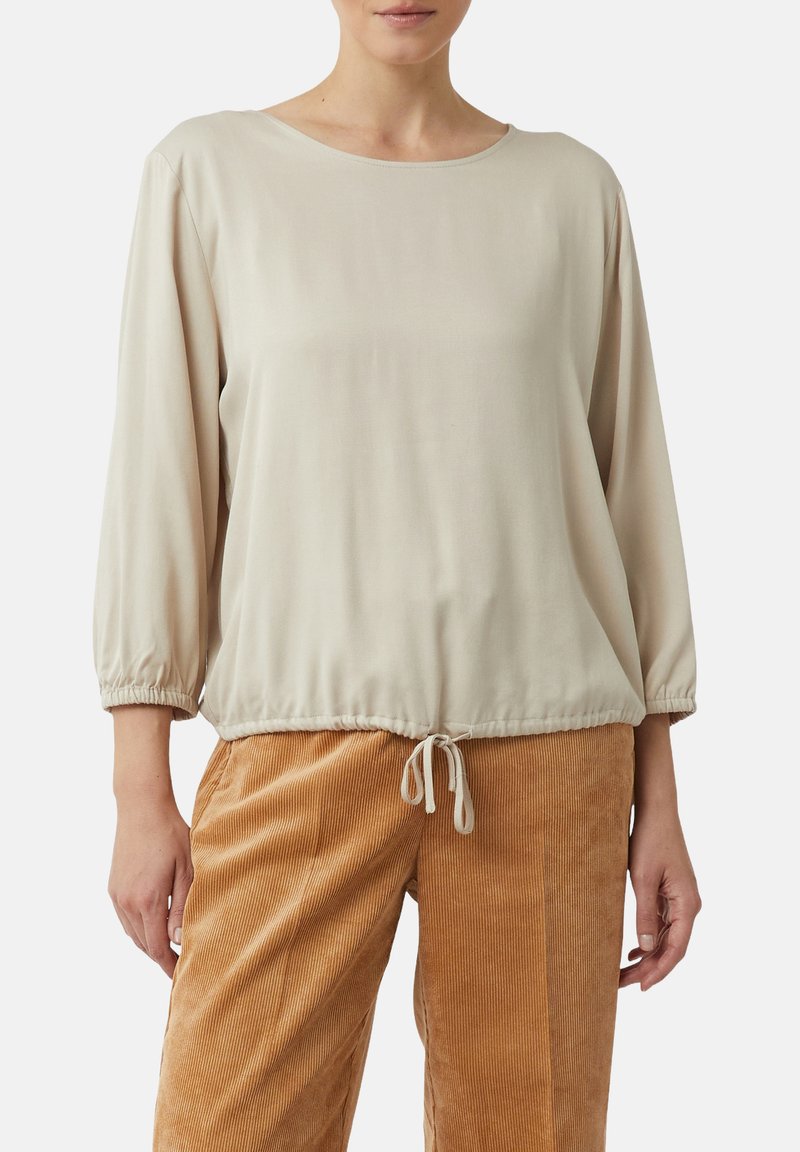 Beige Langarmshirt mit Rundhalsausschnitt und gerafften Bündchen, ausgestattet mit einem Kordelzugsaum und glattem Stoff. Kombiniert mit Cordhosen.
