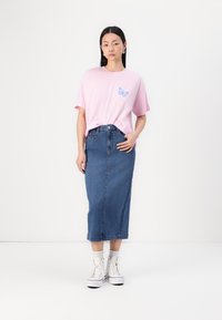 Pink cotton t-shirt with blue butterfly graphic, paired with a knee-length denim skirt. Model wears white sneakers and ankle socks.