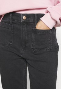 Sorte denimjeans med høyt livdesign, med frontlommer og en kobberknapp i midjen. Glatt tekstur.