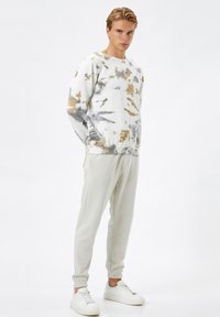 Biały sweter w stylu tie-dye z szarymi i złotymi akcentami, zestawiony z jasnoszarymi dresami i białymi trampkami. Luźny krój i miękka tekstura.