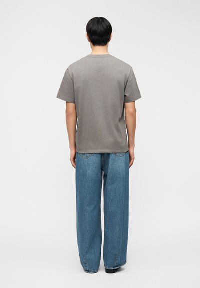 Γκρι βαμβακερό T-shirt με κοντά μανίκια, σε συνδυασμό με μπλε τζιν παντελόνι με φαρδιά μπατζάκια, που διαθέτει κλασικό σχέδιο και ελάχιστες ραφές.