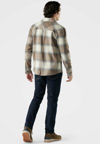 Brun och krämprickig flanellskjorta med knäppning fram, långa ärmar och två bröstfickor, bärs över mörkblå jeans och bruna skor.