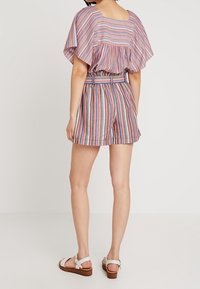 Tenue en tissu rayé comprenant un haut ample avec une taille cintrée et un short assorti. La palette de couleurs inclut le rose, le bleu et le beige.