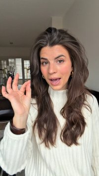 Modell mit langen, welligen braunen Haaren, das einen cremefarbenen gestrickten Pullover trägt. Sie zeigt eine "OK"-Handgeste und befindet sich in einer gut beleuchteten Innenumgebung.