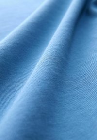 Gros plan sur un tissu bleu clair doux avec une texture fine et des plis visibles créant des ombres douces.